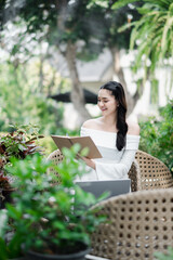 Smiling freelancer works on a clipboard with a laptop on the table, surrounded by lush garden greenery.