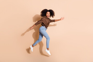 Fototapeta na wymiar Full size photo of charming excited woman dressed brown shirt jeans run empty space astonished staring isolated on beige color background