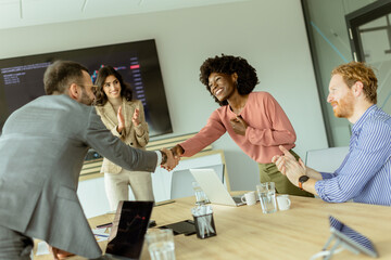Jubilant business professionals celebrating success with a handshake in a modern office meeting room - obrazy, fototapety, plakaty