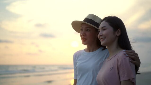 Bisexual lesbian girlfriend woman couple walking on the beach with their arms crossed with rainbow flag. LGBTQ female couple have a romantic moment on the beach. LGBT and homosexual concept.
