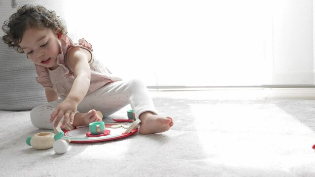 horizontal 4k slow motion video of a little girl playing sitting on the floor of her room with a wooden toy that simulates tea and coffee. Montessori material. Concept of learning, development and ski