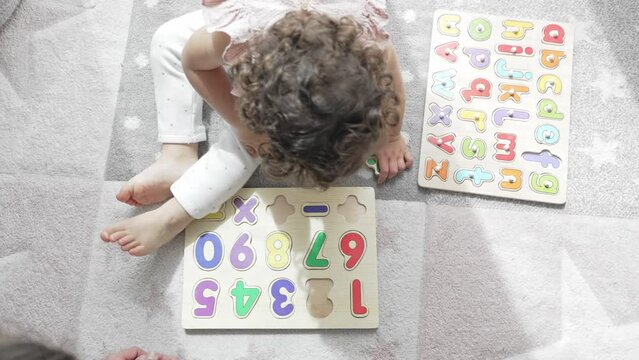 4k slow motion video aerial view of a girl interacting with her mother sitting on the floor of her room with some wooden letter and number puzzles. Montessori methodology and education. development in