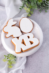 On a gray table there is a plate with ginger Easter cookies in the shape of a hare, egg and letters.