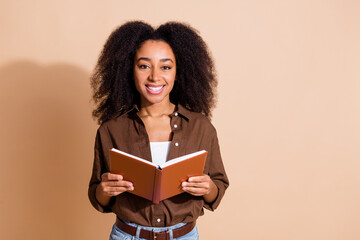 Portrait of adorable smart cute woman with wavy hairstyle dressed brown shirt hold book in hands isolated on beige color background
