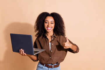 Portrait of attractive woman with wavy hairstyle dressed brown shirt hold laptop showing thumb up isolated on beige color background
