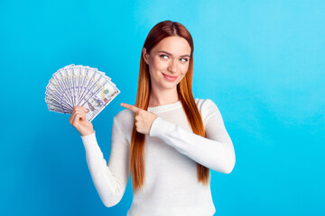 Photo portrait of attractive young woman hold point look money dollars fan dressed stylish white clothes isolated on blue color background