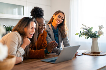 Group of female colleagues using laptop and smiling.