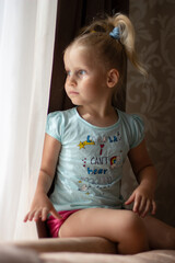 4 year old blonde girl sits by the window and looks out the window
