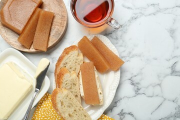 Delicious quince paste, bread, butter and cup of tea on white marble table, flat lay. Space for text