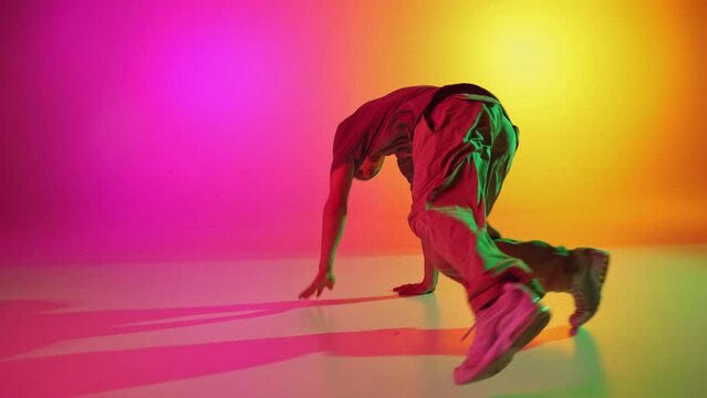 Talented dancer dressed streetwear performing freestyle moves in motion in neon light against gradient pink-yellow background. Concept of art, hobby, sport, creativity, fashion and style, action. Ad