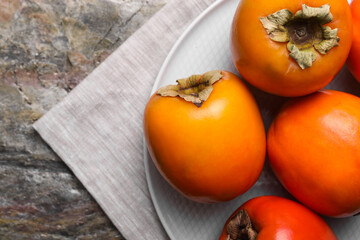 Delicious ripe persimmons on textured table, top view. Space for text