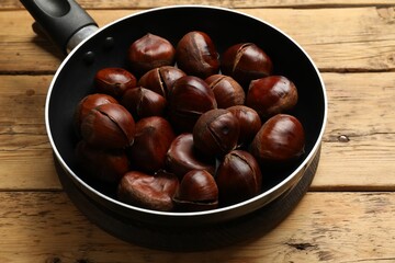 Fresh edible sweet chestnuts in frying pan on wooden table