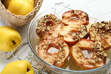 Delicious baked quinces with nuts in bowl and fresh fruits on table, closeup