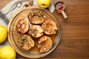 Tasty baked quinces with walnuts and honey in bowl on wooden table, flat lay. Space for text