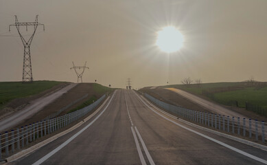 Droga wspinająca się na wzgórze, biegnąca przez pola, o zachodzie słońca. Asfaltowa droga...