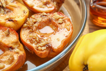 Tasty baked quinces with walnuts and honey in bowl on wooden table, closeup