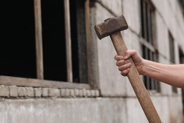Man with sledgehammer near old building outdoors, closeup. Space for text