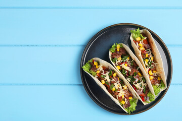 Delicious tacos with meat and vegetables on light blue table, top view. Space for text