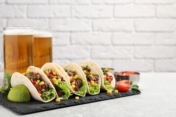 Delicious tacos with meat and vegetables on gray marble table against light brick wall, space for text