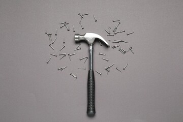 Hammer and metal nails on grey background, top view