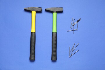 Hammers and metal nails on blue background, top view