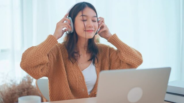 Confident and cheerful asian woman wearing headphones. Young female professional using video call and chatting online from her home. Modern living room. Remote working.	