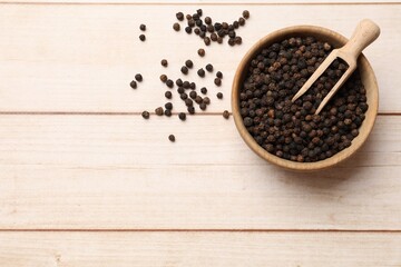 Aromatic spice. Black peppercorns and scoop in bowl on wooden table, top view. Space for text