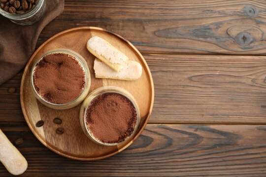 Delicious tiramisu in glasses, coffee beans and cookies on wooden table, flat lay. Space for text