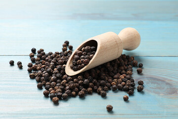 Aromatic spice. Black pepper in scoop on light blue wooden table, closeup