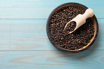 Aromatic spice. Black pepper in bowl and scoop on light blue wooden table, top view. Space for text