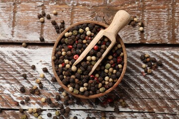 Aromatic spice. Different peppers in bowl and scoop on wooden table, top view