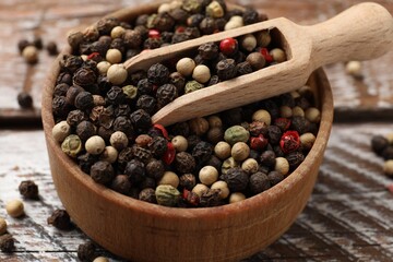 Aromatic spice. Different peppers in bowl and scoop on wooden table, closeup