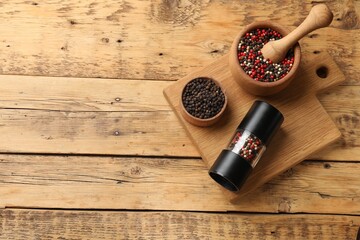 Different peppercorns on wooden table, flat lay. Space for text
