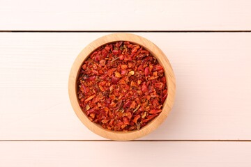 Chili pepper flakes in bowl on white wooden table, top view
