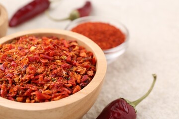 Chili pepper flakes and pods on light textured table, closeup. Space for text
