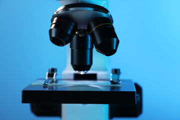 Microscope with glass slide on blue background, closeup