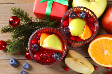Aromatic Sangria drink in glasses, ingredients and Christmas decor on wooden table, flat lay