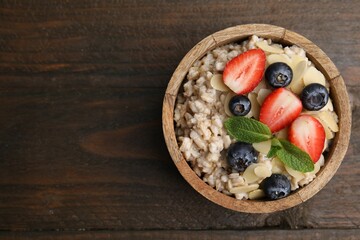 Fototapeta na wymiar Tasty oatmeal with strawberries, blueberries and almond flakes in bowl on wooden table, top view. Space for text