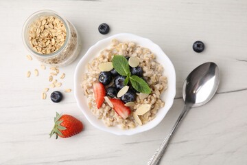 Tasty oatmeal with strawberries, blueberries and almond petals in bowl served on white wooden...