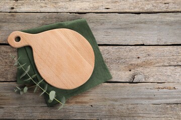 Cutting board, eucalyptus branch and napkin on wooden table, top view. Space for text