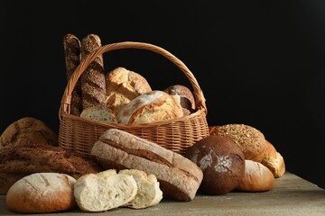 Wicker basket with different types of fresh bread on wooden table