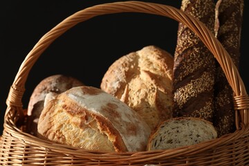 Wicker basket with different types of fresh bread against black background