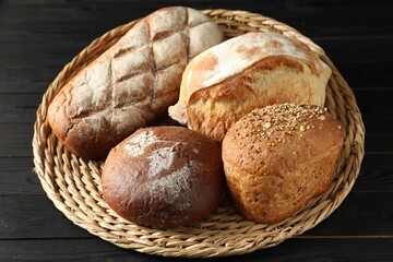Wicker basket with different types of fresh bread on black wooden table