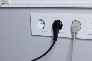 Power sockets and electric plugs on grey wall, closeup