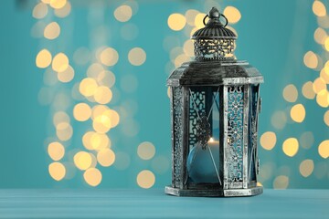 Traditional Arabic lantern on table against light blue background with blurred lights. Space for...