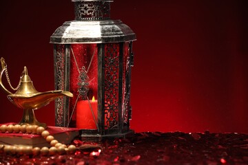 Arabic lantern, Quran, misbaha and Aladdin magic lamp on shiny red table. Space for text