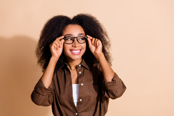 Portrait of smart woman with wavy hairdo dressed brown shirt touch glasses look at offer empty...