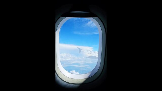 View of an airplane wing from a porthole against a blue sky background. A passenger plane flies above the clouds in the morning light. The concept of traveling by air. Fear of heights, aerophobia. 4K