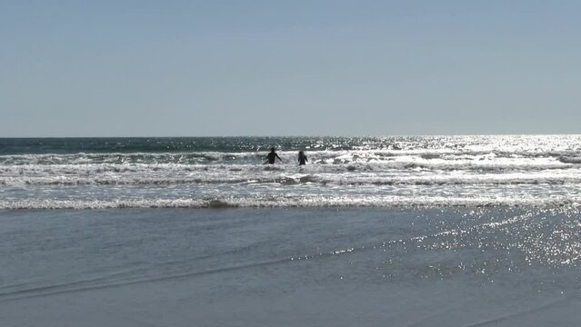 Silhouette Man And Woman With Surfboards Wading Into Ocean With Blue Sky Oceanside California
