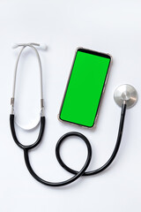 Stethoscope on a white background and a smartphone with a green screen, top view. Medical...
